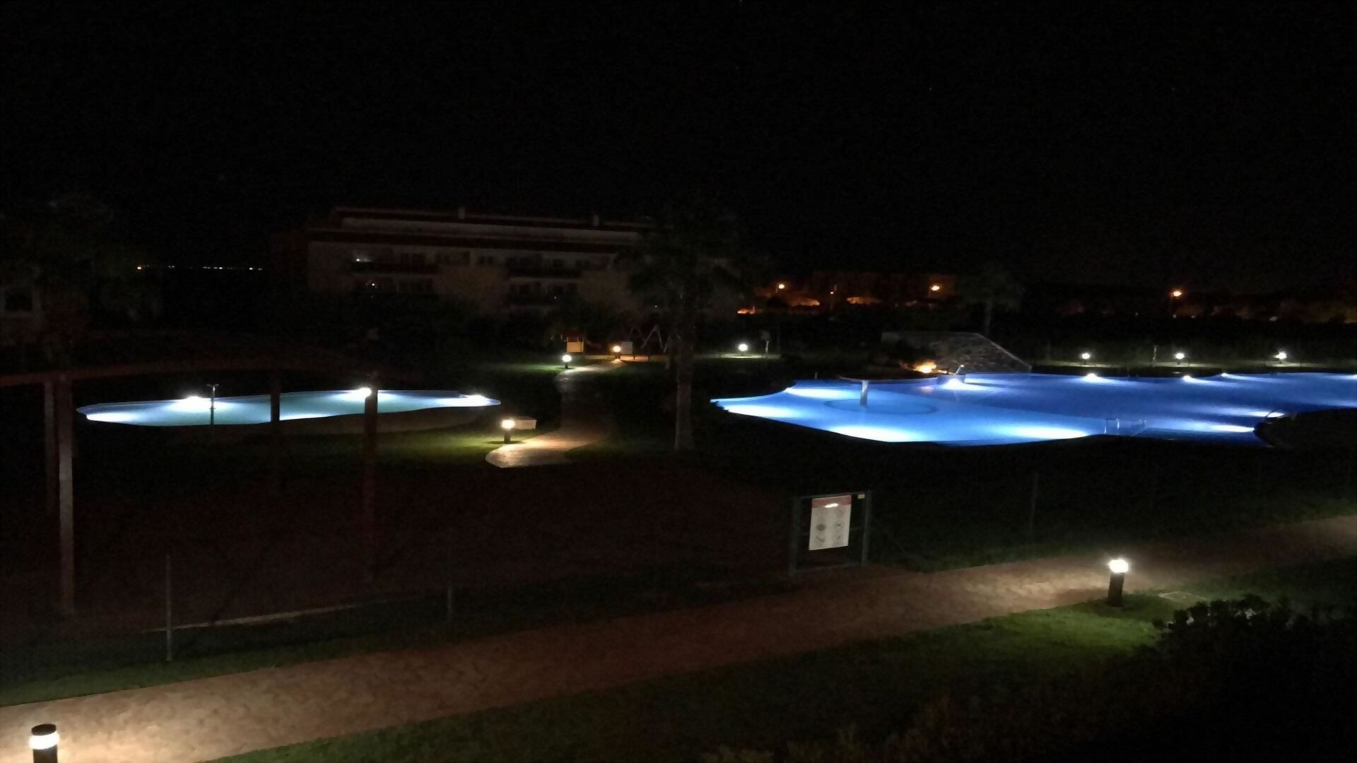A nighttime view of a swimming pool complex with multiple pools and surrounding pathways.