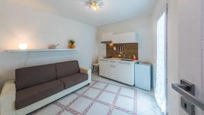 Um espaço de estar compacto com sofá, cozinha compacta e piso de azulejos.