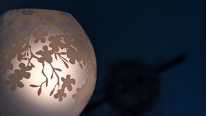 Uma luminária esférica com desenhos recortados de flores, sobre um fundo escuro.