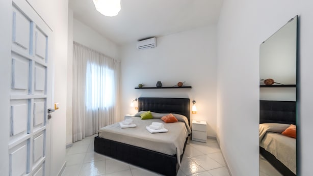 Quarto moderno com uma cama grande, mesa de cabeceira, espelho e guarda-roupa.
