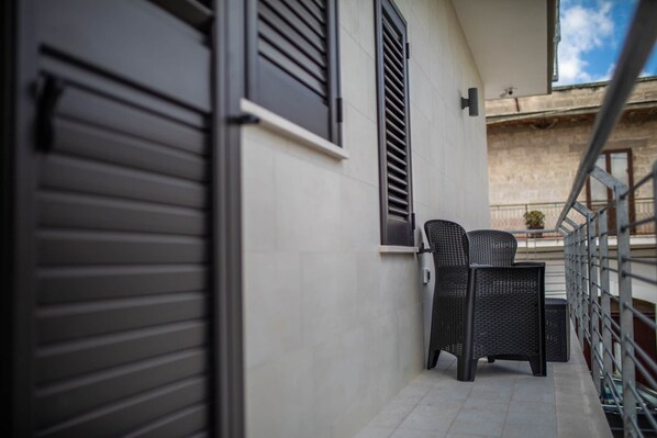 A balcony with a closed shutter, a wicker chair, and a small table. - Angela Rosa House (Carovigno)
