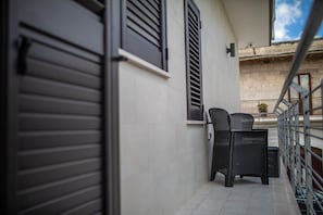A balcony with a closed shutter, a wicker chair, and a small table. - Angela Rosa House (Carovigno)