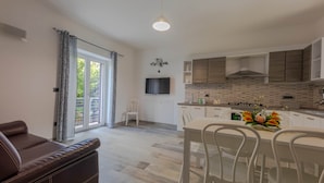 A modern kitchen with a dining area, a sofa, and a TV. - Angela Rosa House (Carovigno)