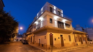A multi-story building with a balcony on the upper floor, a visible door, and a street with parked cars. - Angela Rosa House (Carovigno)