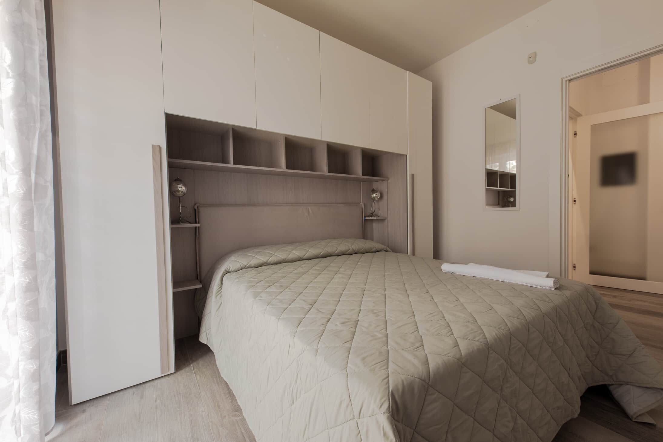 Un dormitorio con cama, estanterías empotradas, un espejo y un armario.