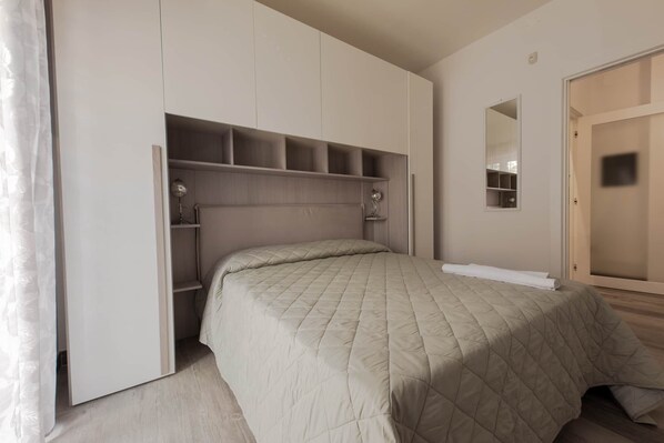 A bedroom with a bed, built-in shelving, a mirror, and a wardrobe. - Angela Rosa House (Carovigno)