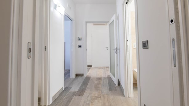 A corridor with white doors, a light switch, and a thermostat on the wall. - Angela Rosa House (Carovigno)
