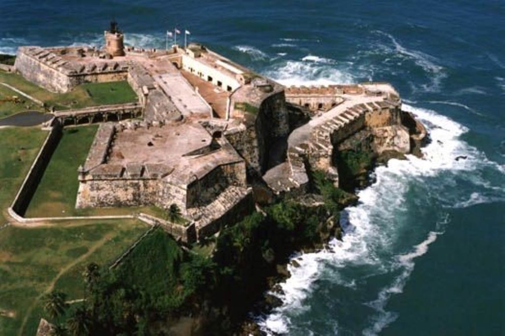 A coastal fortification with a central tower, surrounded by walls and a moat.