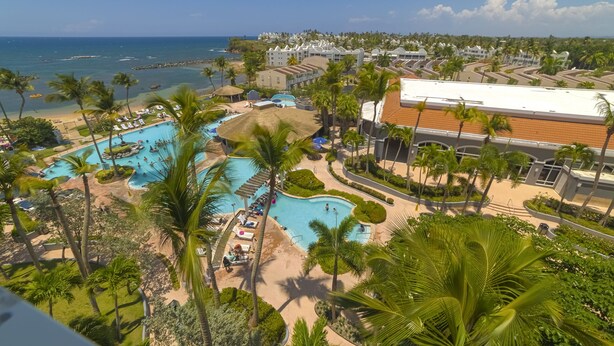 Ein Resort mit mehreren Swimmingpools, Palmen und Blick auf den Ozean.