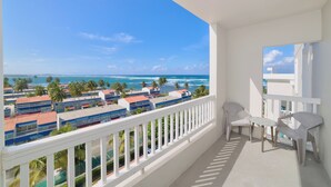 Ein Balkon mit Blick auf das Meer und Palmen, weiße Geländer und zwei Stühle.