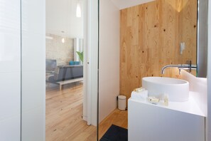 Un baño moderno con un revestimiento de madera en una pared, un lavamanos blanco y un box de ducha de vidrio.