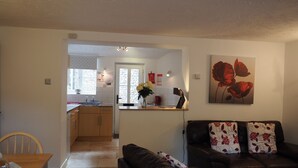 Ein Wohnzimmer mit Ledersofa, einem Esstisch und einer Küche im Hintergrund.