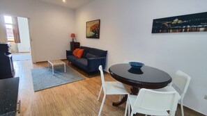 Ein modernes Wohnzimmer mit einer Couch, einem Esstisch mit Stühlen, einem Couchtisch, einer Lampe und einem Bild an der Wand.