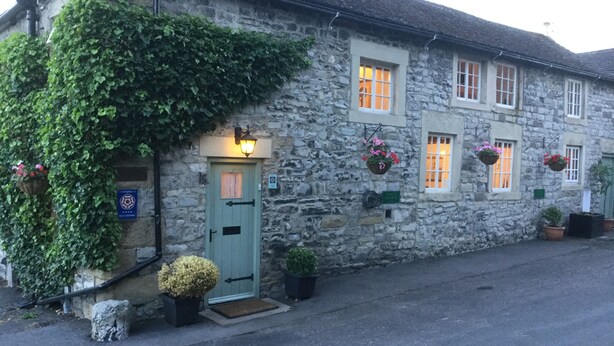 A stone building with a green door, multiple windows, and hanging flower baskets.