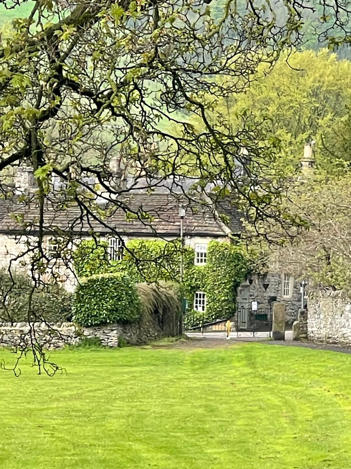 A stone building with a traditional roof, surrounded by a well-maintained lawn and dense foliage.