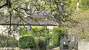 A stone building with a traditional roof, surrounded by a well-maintained lawn and dense foliage.