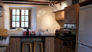 A kitchen with wooden cabinets, a large window, a sink, stools, a stove, and a refrigerator.