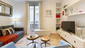 Un salon moderne comprenant un canapé, deux fauteuils, une table basse, un téléviseur et une bibliothèque.