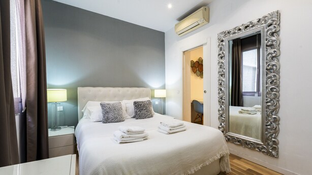 Un lit bien fait, avec des oreillers et des serviettes pliées, une lampe de chevet et un grand miroir décoratif accroché au mur.