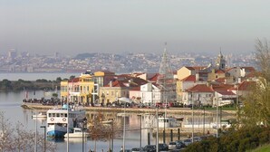 Un paisaje urbano frente al agua, con edificios, una destacada aguja de iglesia y un muelle con barcos.