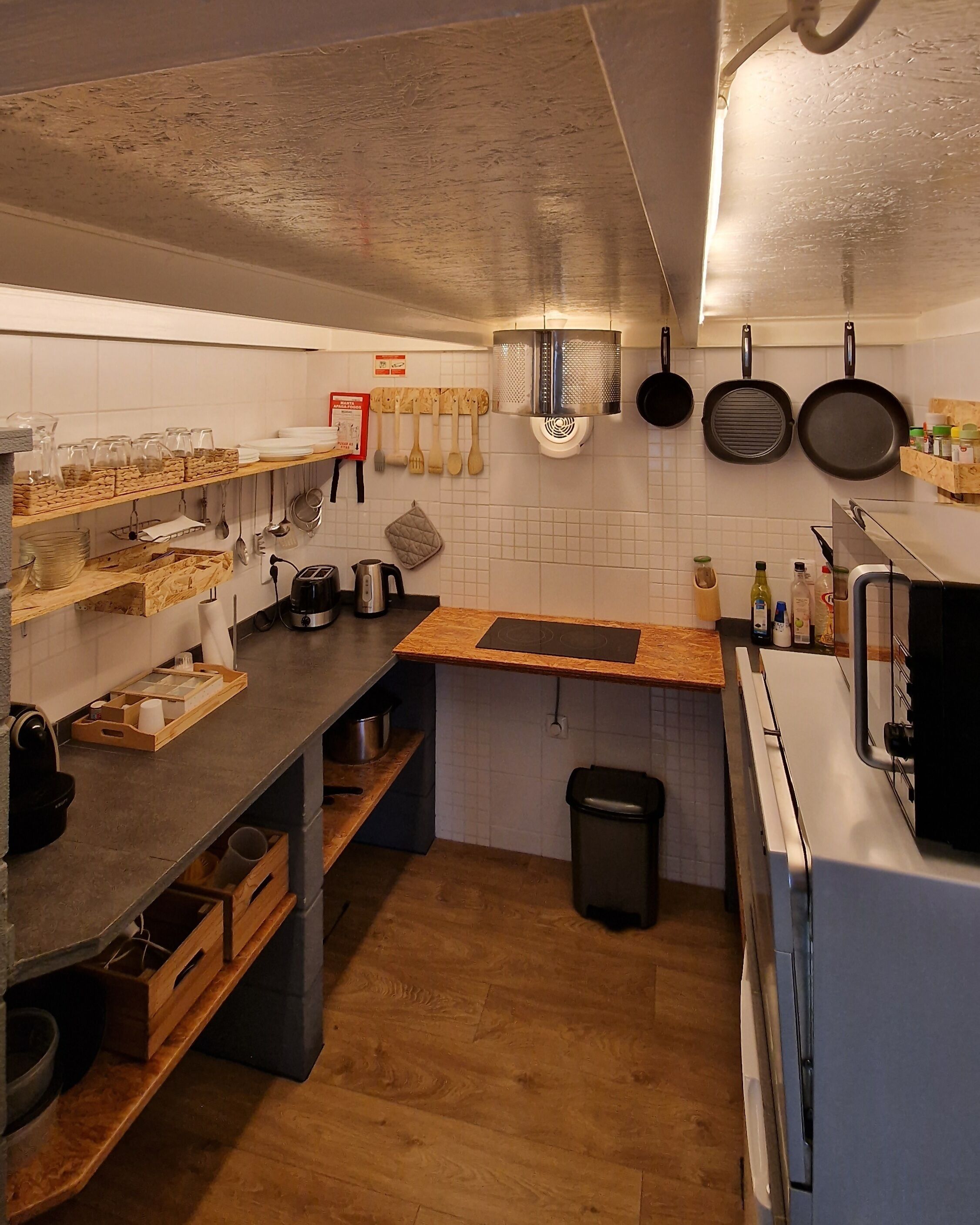 Une cuisine dotée de plans de travail en bois, d’une machine à café, d’une poubelle et d’ustensiles suspendus.