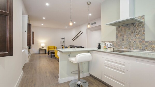A modern kitchen with white cabinetry, a bar area, and a yellow chair. - Garnata Luxury apartment in Granada. (Granada)
