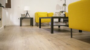 A modern living room with a wooden floor, a black coffee table, yellow armchairs, and a small side table with a lamp. - Garnata Luxury apartment in Granada. (Granada)