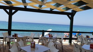 Ein überdachter Außenbereich zum Sitzen mit Tischen und Stühlen, mit Blick auf das Meer.