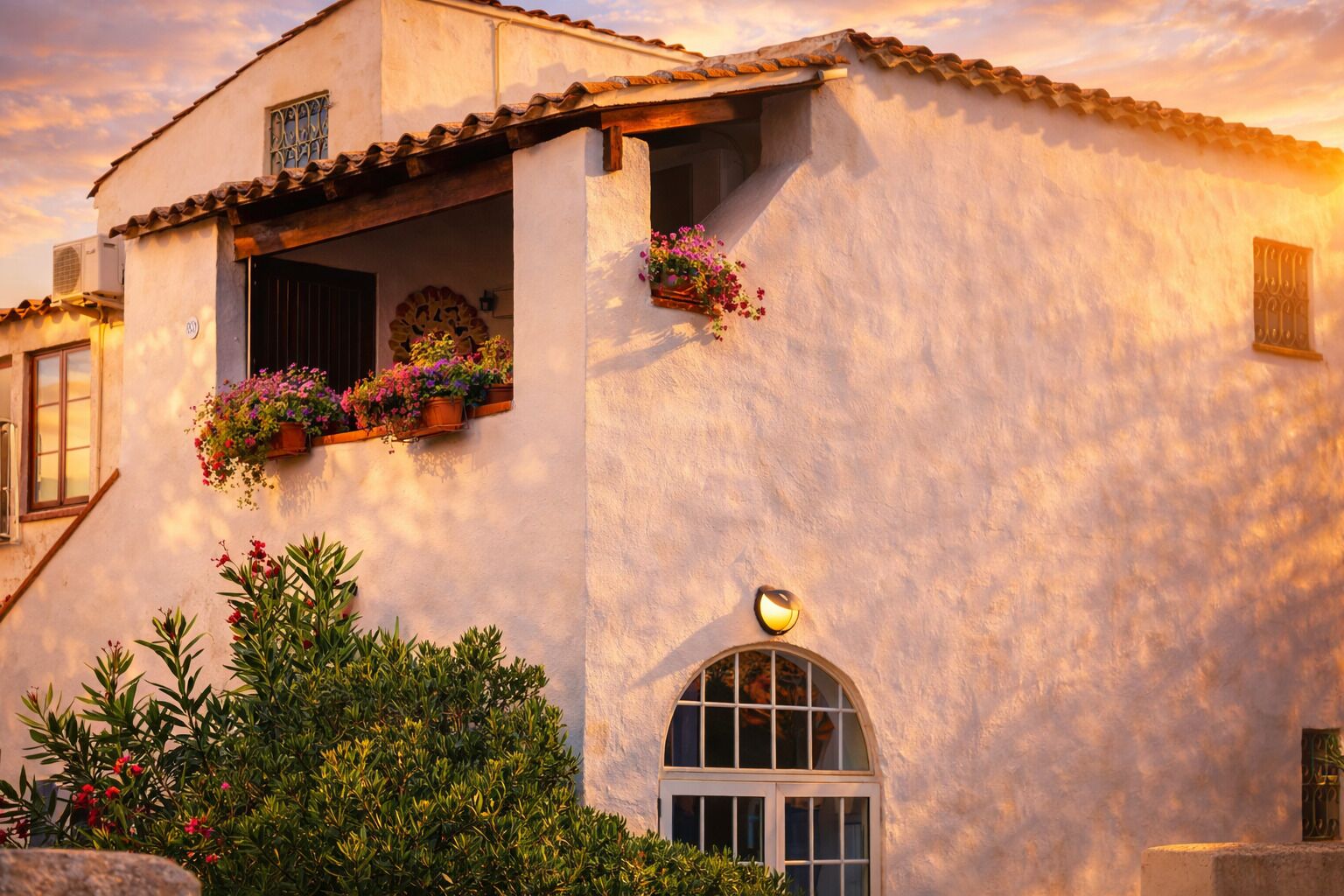 A building with a stucco exterior, a balcony with potted plants, and a window with a decorative grille.