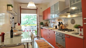 Een moderne keuken met rode kastjes, roestvrijstalen apparatuur en een eethoek met een tafel en stoelen.