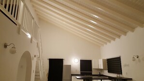 Una cocina con techo alto, paredes blancas, encimera negra y un refrigerador.