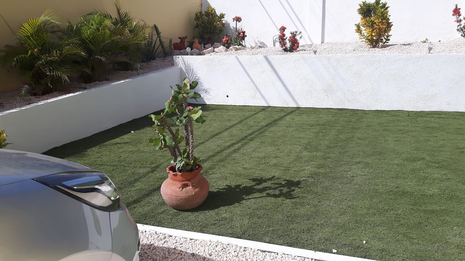 A section of a building with artificial grass, a potted plant, and a car.