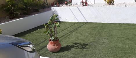 A section of a building with artificial grass, a potted plant, and a car.