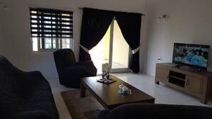 Una sala de estar con sofá, sillón, mesa de centro, televisión y ventana con cortinas.