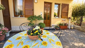 A patio with a round table, potted plants, and a yellow wall with wooden shutters. - Casa Rosalia patio apartment (Tremosine)