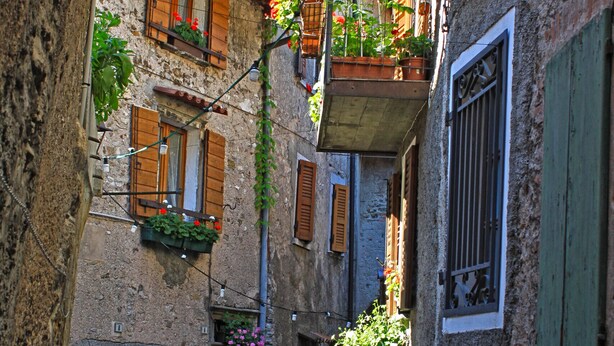 A narrow street with stone buildings, wooden shutters, and flower boxes on balconies. - Casa Rosalia patio apartment (Tremosine)