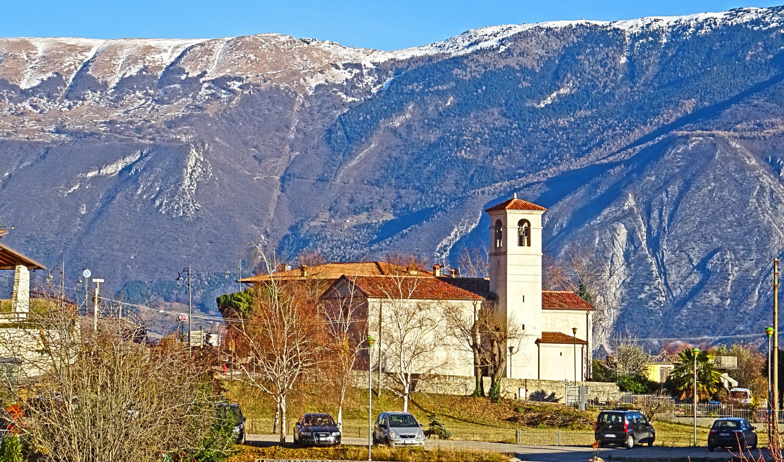 Une église dotée d’un clocher, entourée de montagnes et de voitures garées.