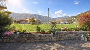 A stone wall with potted plants, a metal fence, and houses in the background. - Casa Rosalia patio apartment (Tremosine)