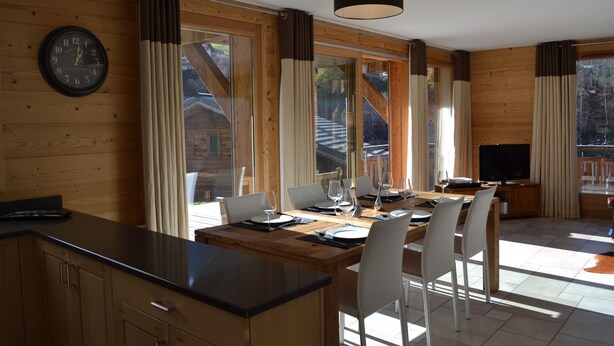 Une cuisine moderne avec un plan de travail en bois, un coin repas avec une table dressée pour quatre personnes, et un téléviseur en arrière-plan.