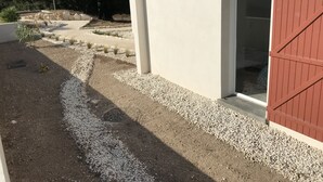 Un edificio con una puerta roja, una ventana y un camino de grava que lo conduce.