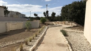Un sendero pavimentado bordeado por grava y pequeñas plantas, que conduce a un edificio con fachada blanca y una entrada porticada.