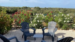 Mesa y sillas en un espacio al aire libre, rodeado de grava y plantas con flores.