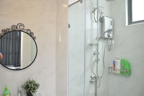 Une salle de bain dotée d’une douche à parois de verre, d’un miroir rond orné d’un cadre décoratif et d’une étagère contenant des articles de toilette.
