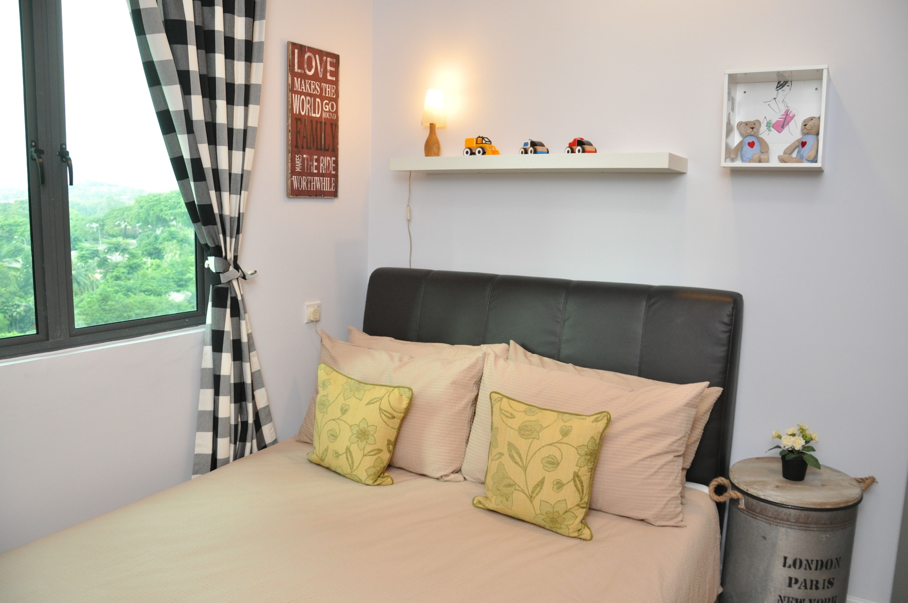 Ein Schlafzimmer mit einem Bett, karierten Vorhängen, einem Kopfteil, einem Regal mit Spielzeug und einer Wand mit einem Schild.