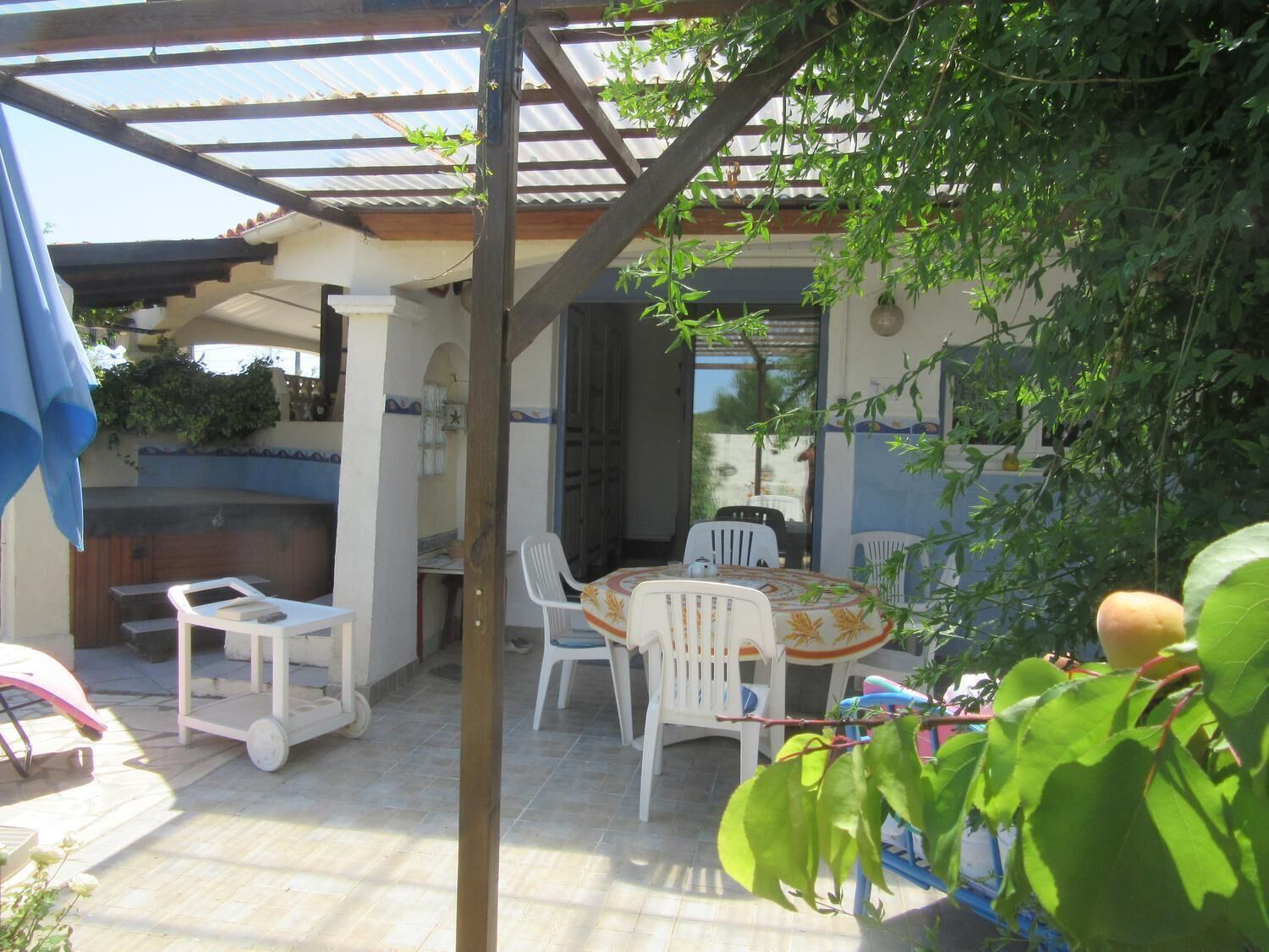 Un patio couvert avec une table et des chaises, un barbecue et une chaise blanche recouverte d’une nappe à motifs floraux.