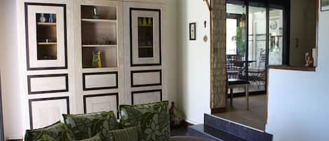 A living room with a sofa, patterned cushions, a cabinet with glass doors, and a view of an outdoor patio area.