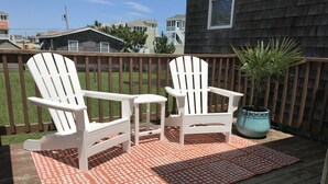 Eine Terrasse mit zwei Adirondack-Stühlen, einem Blumentopf und einem gemusterten Teppich.