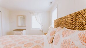 Ein Schlafzimmer mit einem Bett, einem Nachttisch, einem Spiegel und einem Fenster mit Vorhängen.