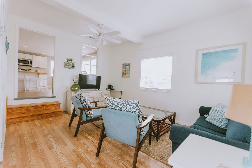 A modern living room with a sofa, chairs, a TV, and a kitchen in the background.