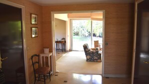 A hallway with a door leading to a room, a chair, a small table, and a window with a view of the outdoors. - rent house in St Briac near golf and beaches, 9 people (Saint-Briac-sur-Mer)